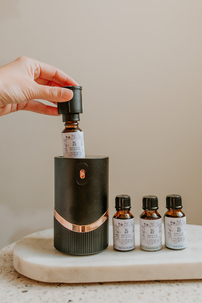 Hand holding a black essential oil diffuser with four bottles on a marble surface.