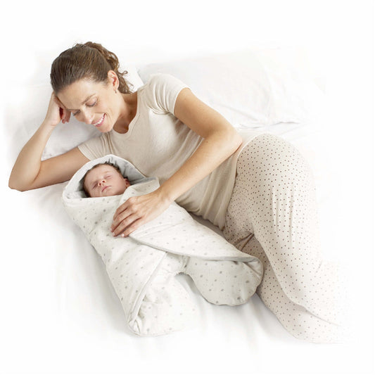 Woman lying on a bed with a baby wrapped in a blanket