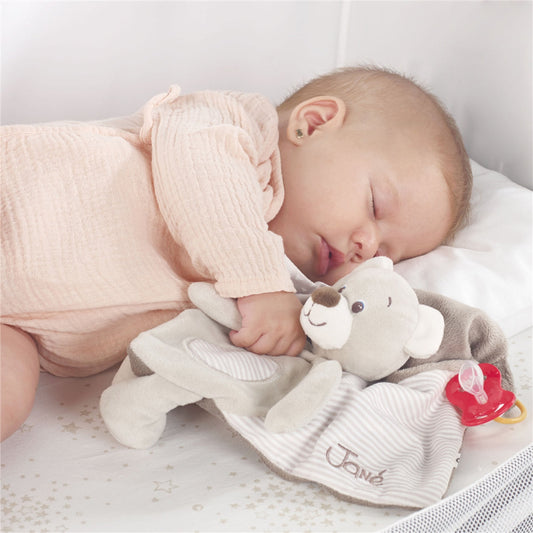 Baby sleeping with a soft toy and pacifier on a white blanket