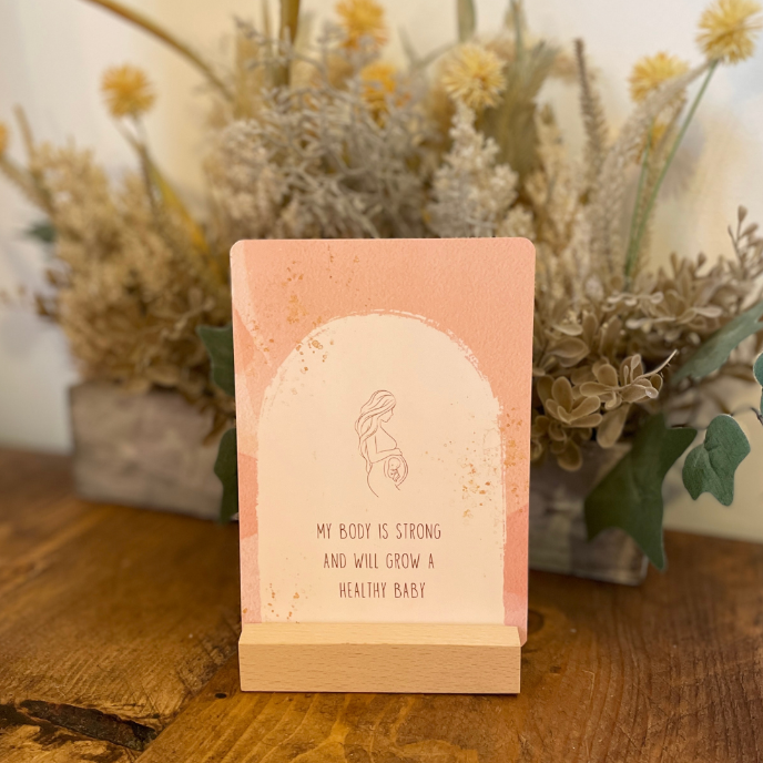 Pink card with text on a wooden stand in front of dried plants