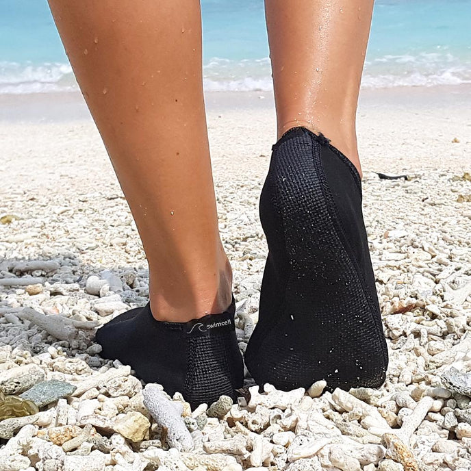 Person wearing black toe-separated socks on a pebbly beach.