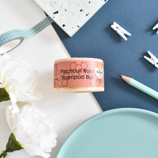 Patchouli Rosa shampoo bar on a white surface with flowers and stationery items.