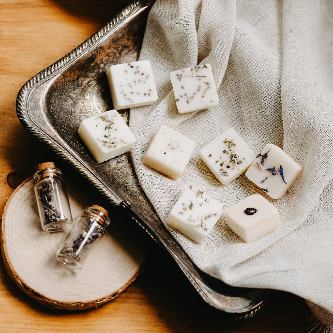 Square soap bars with natural elements on a metal tray with a textured cloth background