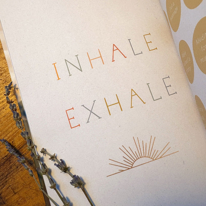 Notebook with 'INHALE EXHALE' text and lavender flowers on a wooden surface