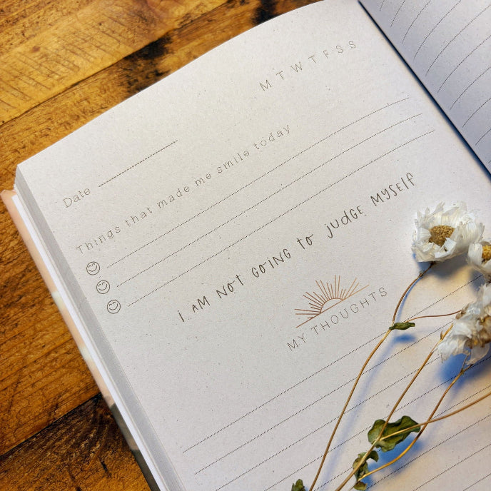 Open notebook with a motivational quote on a wooden surface with flowers.