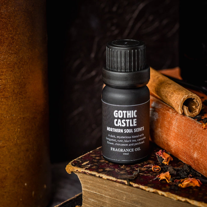 Bottle of Gothic Castle fragrance oil on a dark background with books and candles.