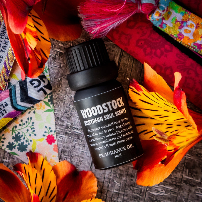 Woodstock Northern Soul Scents fragrance oil bottle on a textured surface with colorful fabrics and flowers.