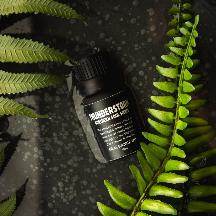 Bottle of 'Thunderstorm' fragrance oil surrounded by green leaves on a dark textured background