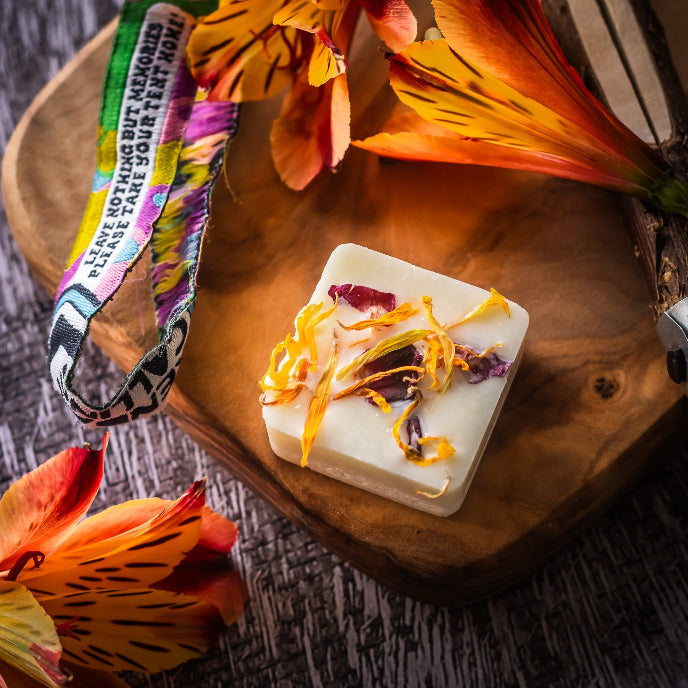 Bar of soap with floral elements on a wooden surface with flowers around