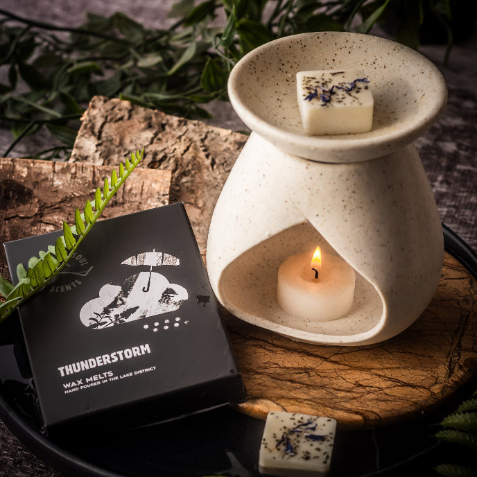 Wax melter with a lit candle and 'Thunderstorm' wax melts packaging on a wooden surface.