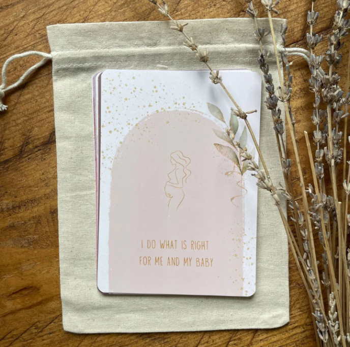 Card with a silhouette of a woman and text on a pink background, placed on a textured fabric pouch with lavender flowers.