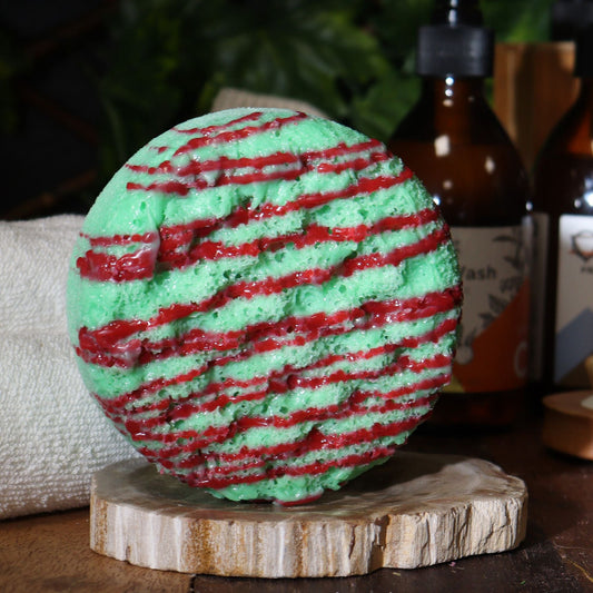 Green and red striped bath bomb on a wooden stand with bottles in the background