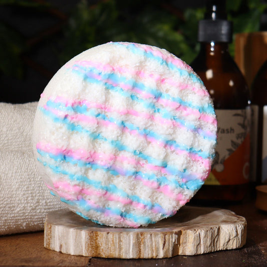 Bath bomb with pink and blue stripes on a wooden stand with bottles in the background