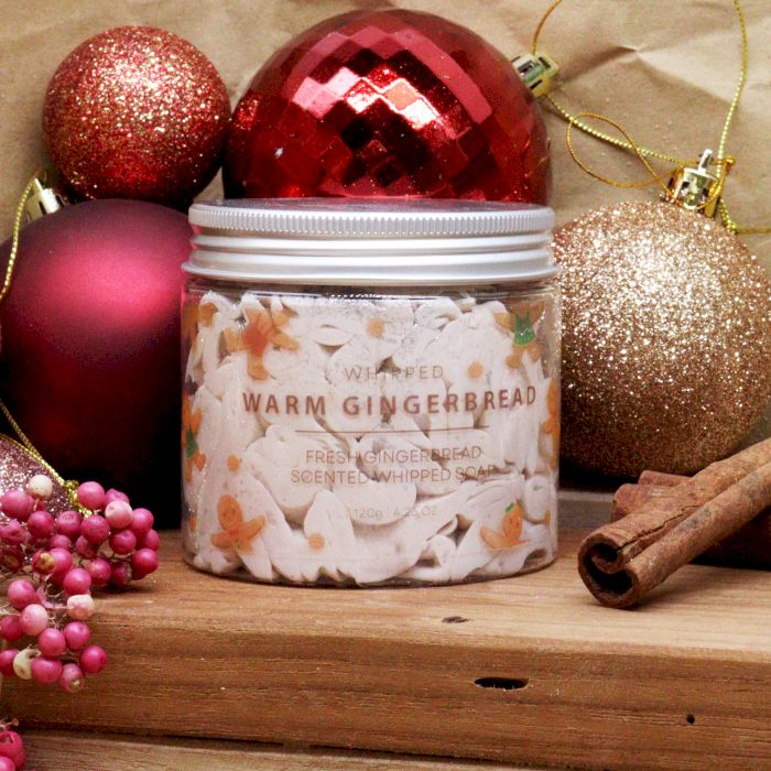 Jar of whipped cream labeled 'Warm Gingerbread' with Christmas ornaments and cinnamon sticks on a wooden surface.