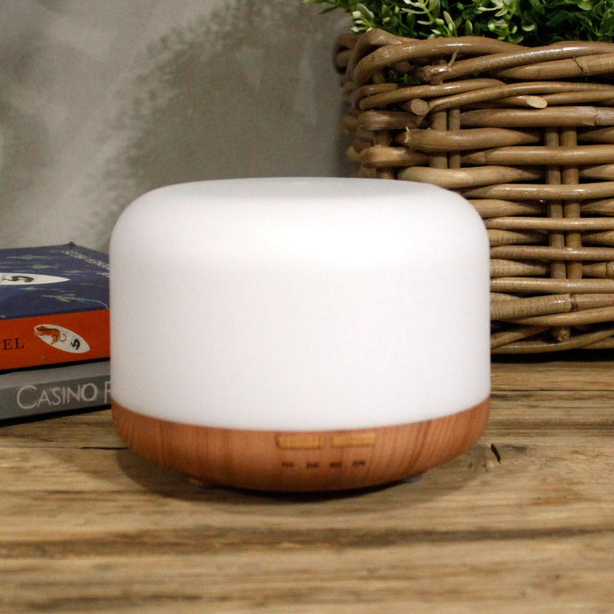 White and wooden diffuser on a wooden surface with books and a basket in the background