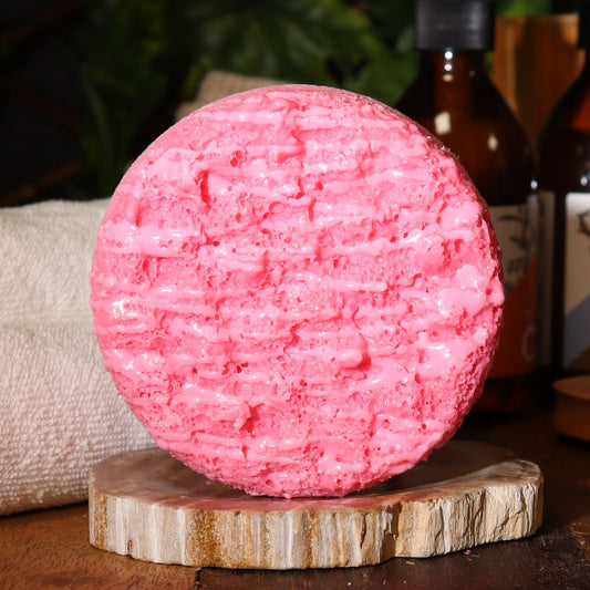 Pink textured soap bar on a wooden stand with bottles in the background