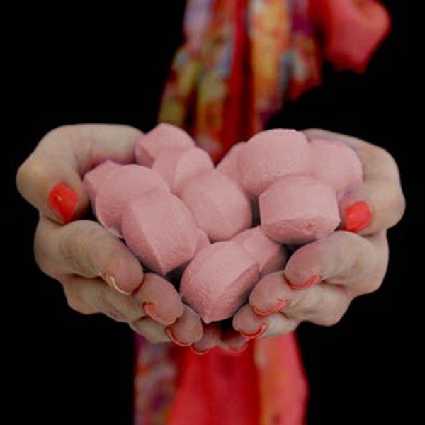 Pink marshmallows held in hands with red nail polish against a dark background