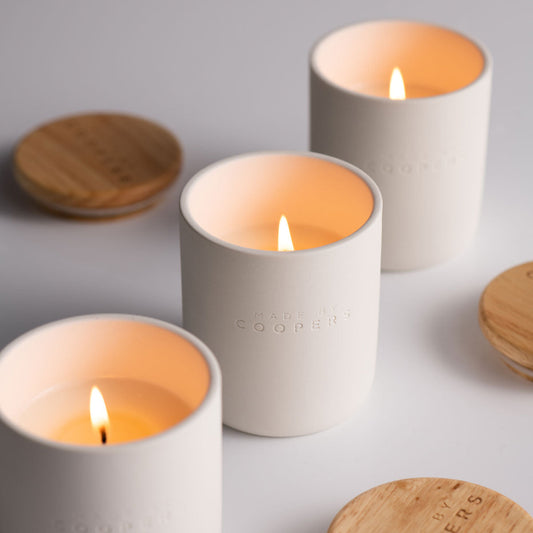 Three lit candles in white containers with wooden lids on a light gray background