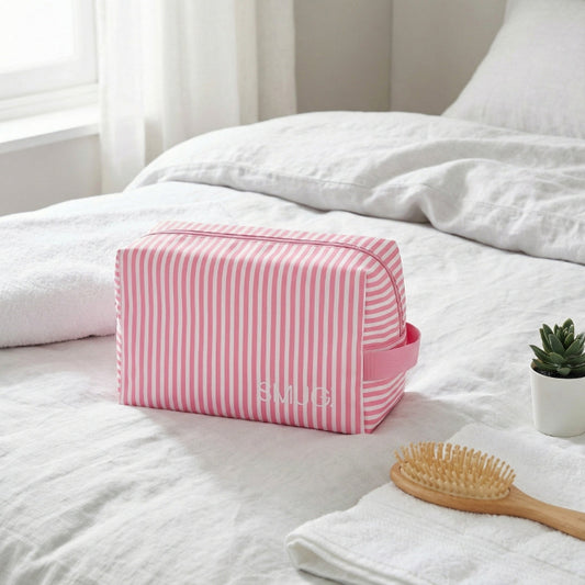 Pink striped toiletry bag on a bed with a plant and hairbrush in the background
