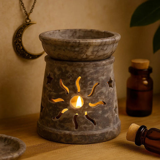 Decorative stone oil burner with sun design on a wooden surface, surrounded by bottles and a moon pendant.