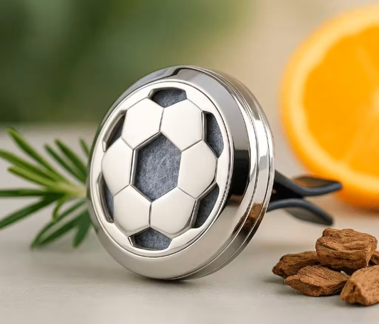 Metallic soccer ball-shaped object on a surface with leaves and an orange in the background