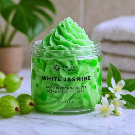 Green whipped soap in a jar with 'Ancient Wisdom' branding, surrounded by gooseberries and flowers.